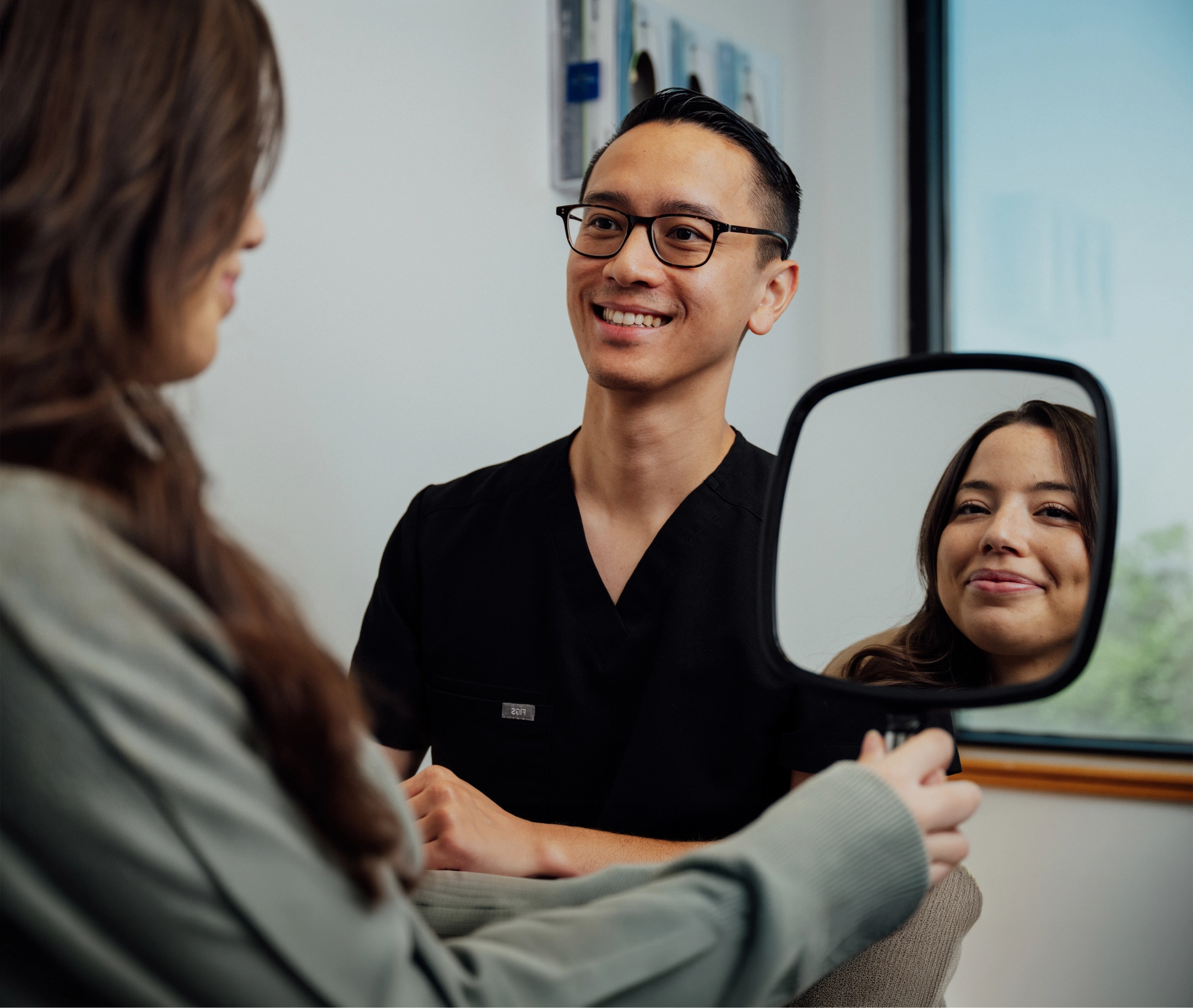 Patient examining smile in mirror while consulting with dentist in modern dental office
