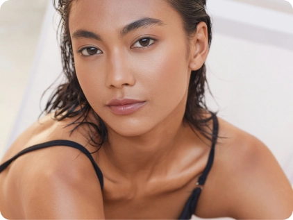 Woman with glowing skin and wet hair in black tank top looking at camera with natural makeup