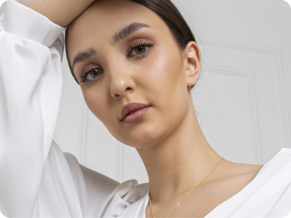 Woman with glowing skin and natural makeup wearing white shirt against neutral background