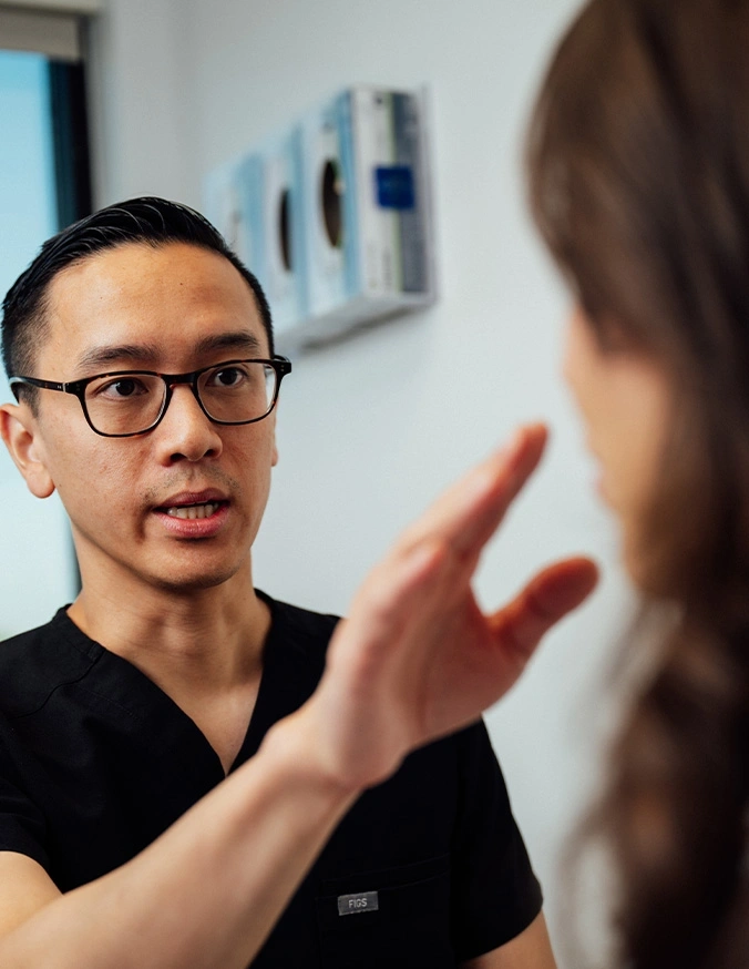 Two professionals having an engaged conversation in modern office setting, one wearing glasses gesturing while speaking