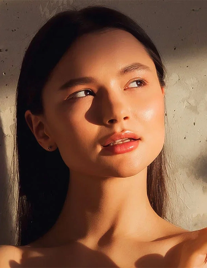 Woman with natural makeup in golden sunlight against textured wall, beauty portrait with warm glow