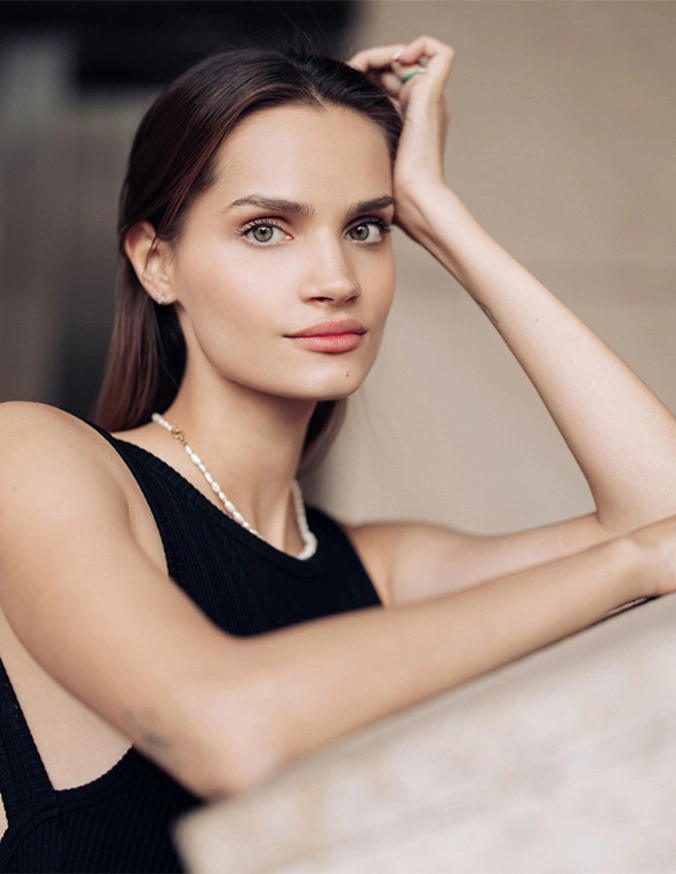 Professional woman in black sleeveless top with natural makeup posing elegantly with hand on forehead