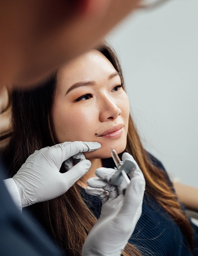 Cosmetic professional in white gloves administering dermal filler injection to woman's chin area during aesthetic treatment