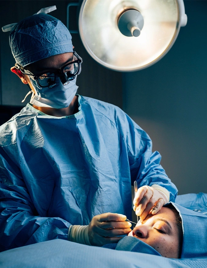 Surgeon performing cosmetic procedure on patient under surgical light in operating room