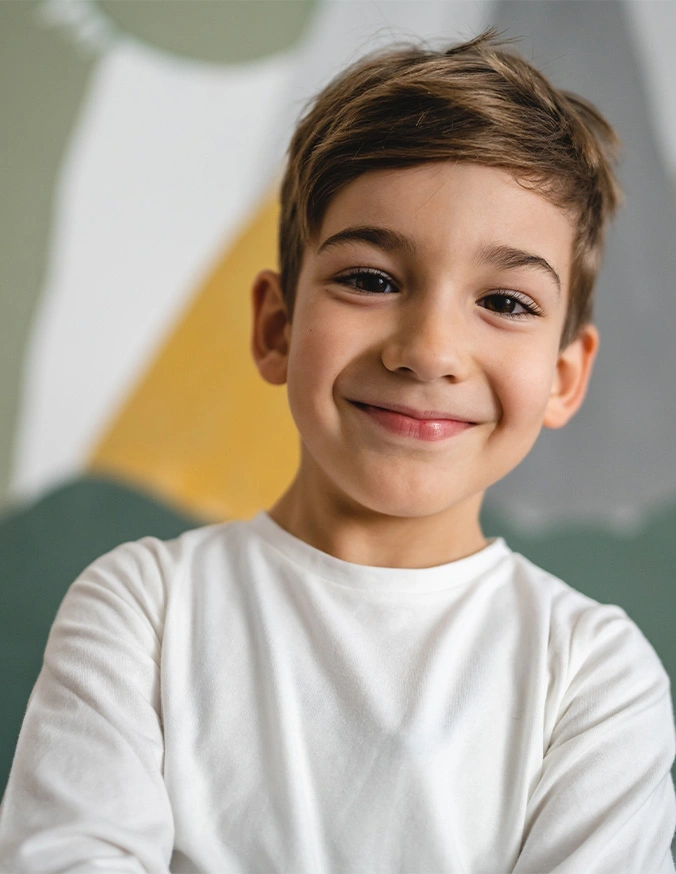 Happy young boy in white t-shirt smiling at camera with natural lighting and colorful background