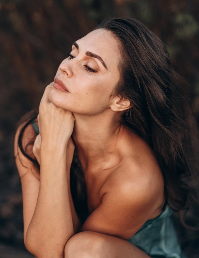 Woman with dark hair in elegant pose touching neck, soft natural lighting portrait photography