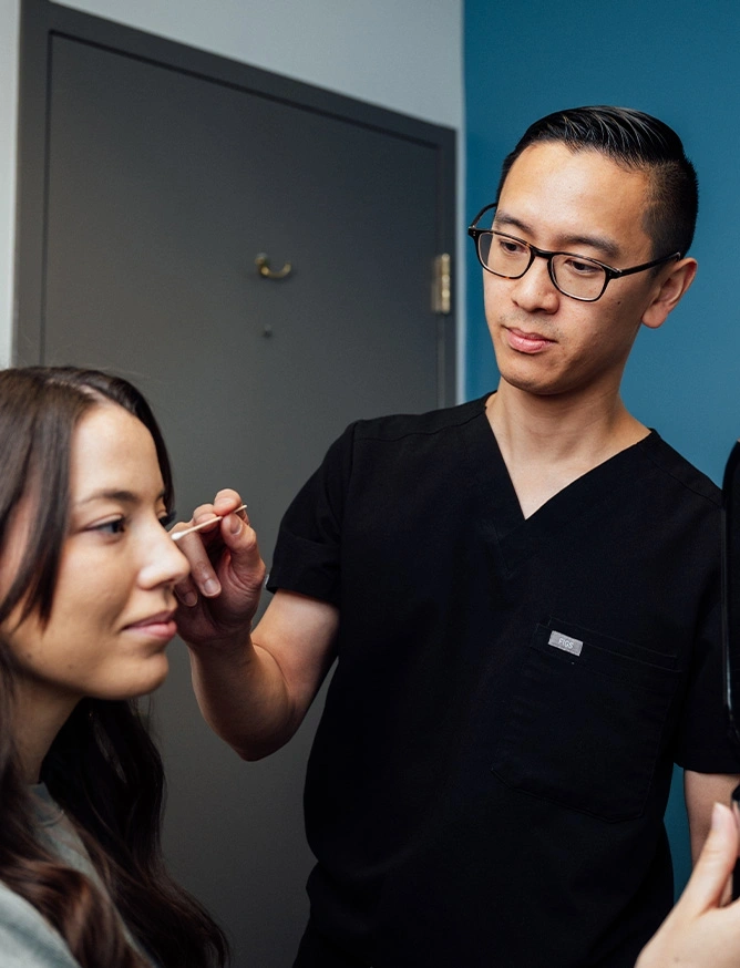 Male cosmetic injector in black scrubs administering Botox treatment to female patient in medical clinic