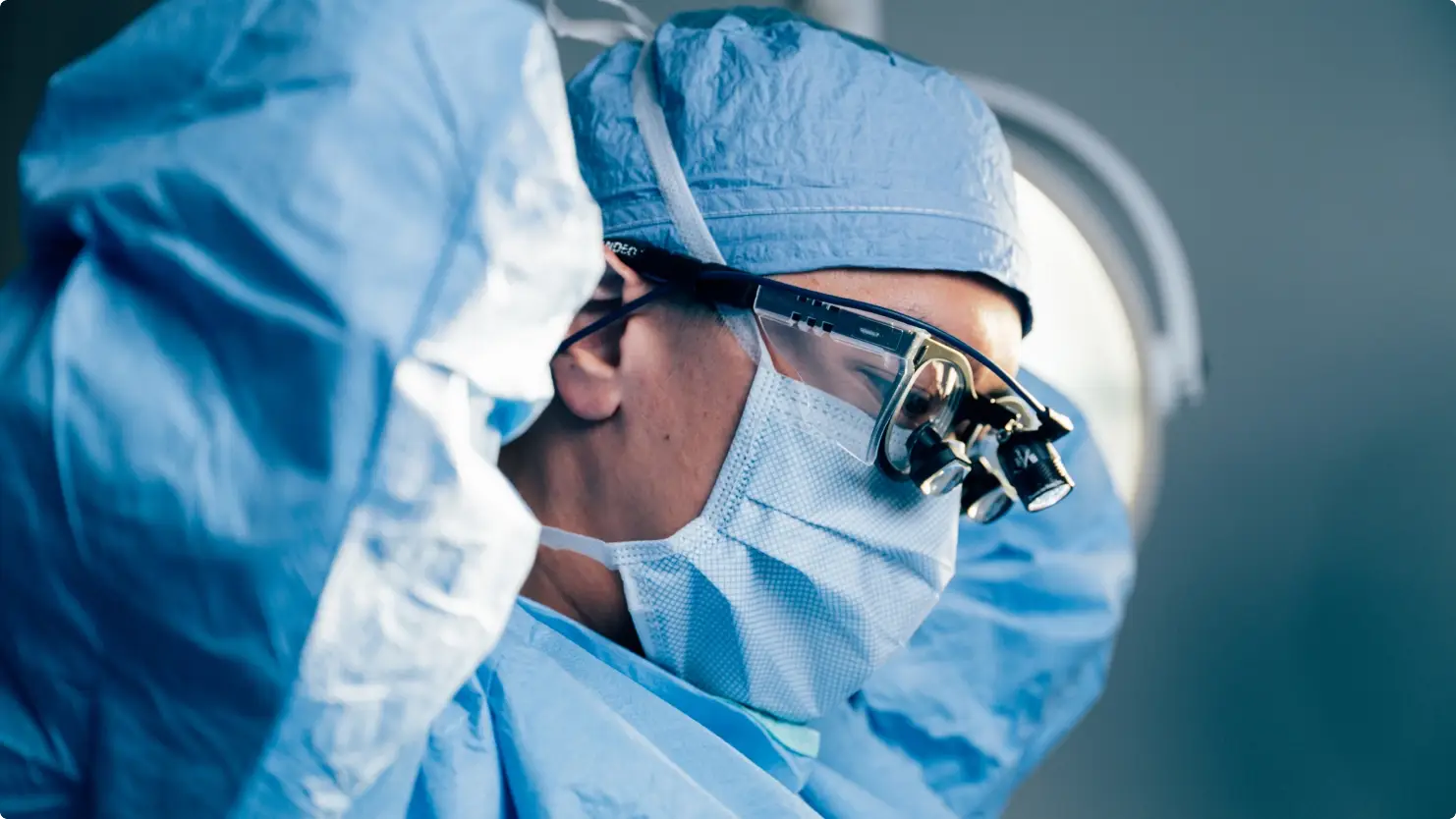 Surgeon wearing surgical loupes and protective equipment performing medical procedure in operating room