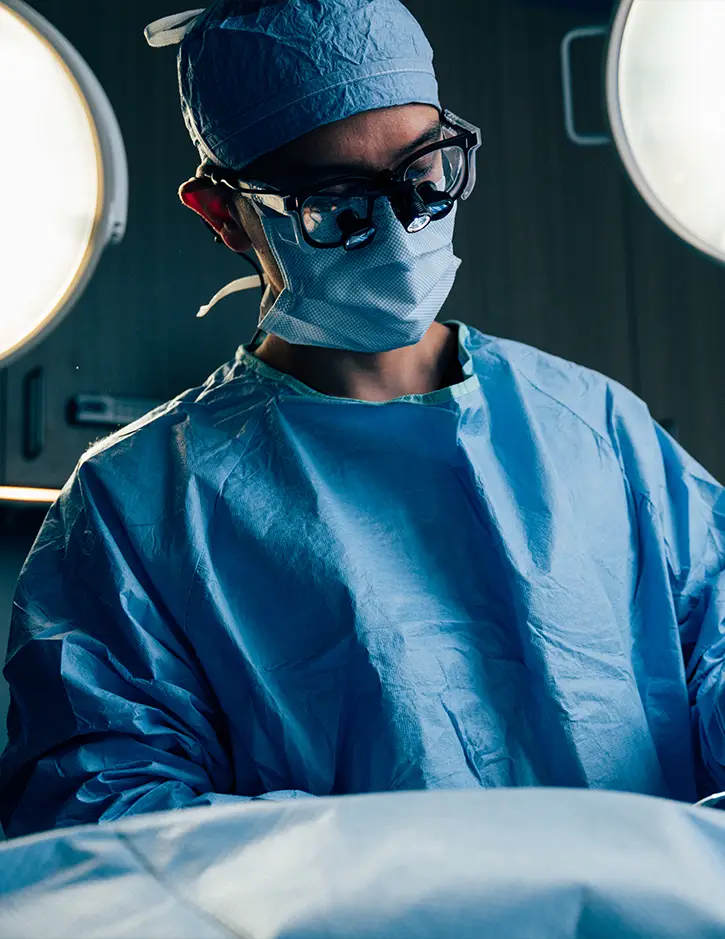 Surgeon in blue scrubs and protective eyewear performing medical procedure in operating room
