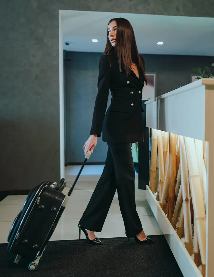 Professional woman in business suit walking with rolling luggage through modern medical facility corridor